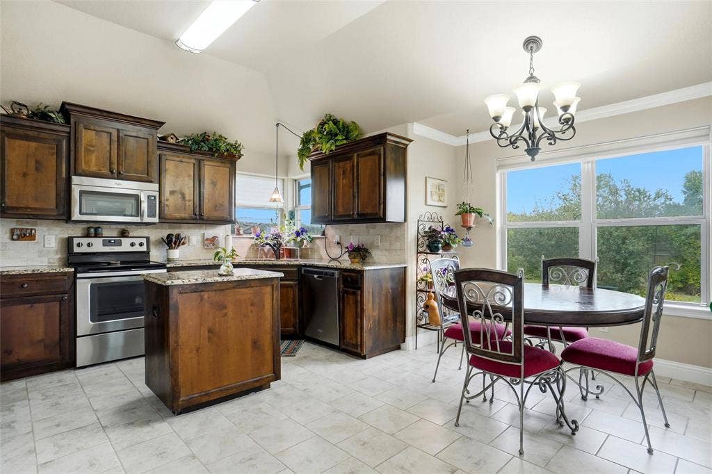 Kitchen featuring stained wood cabinetry, stone countertops, stainless steel appliances, a center island, and a chandelier-lit dining area