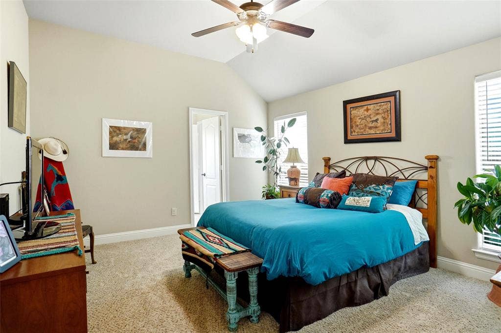 Vaulted ceiling featuring a central wooden ceiling fan with integrated lighting, neutral wall finishes, and carpeted flooring