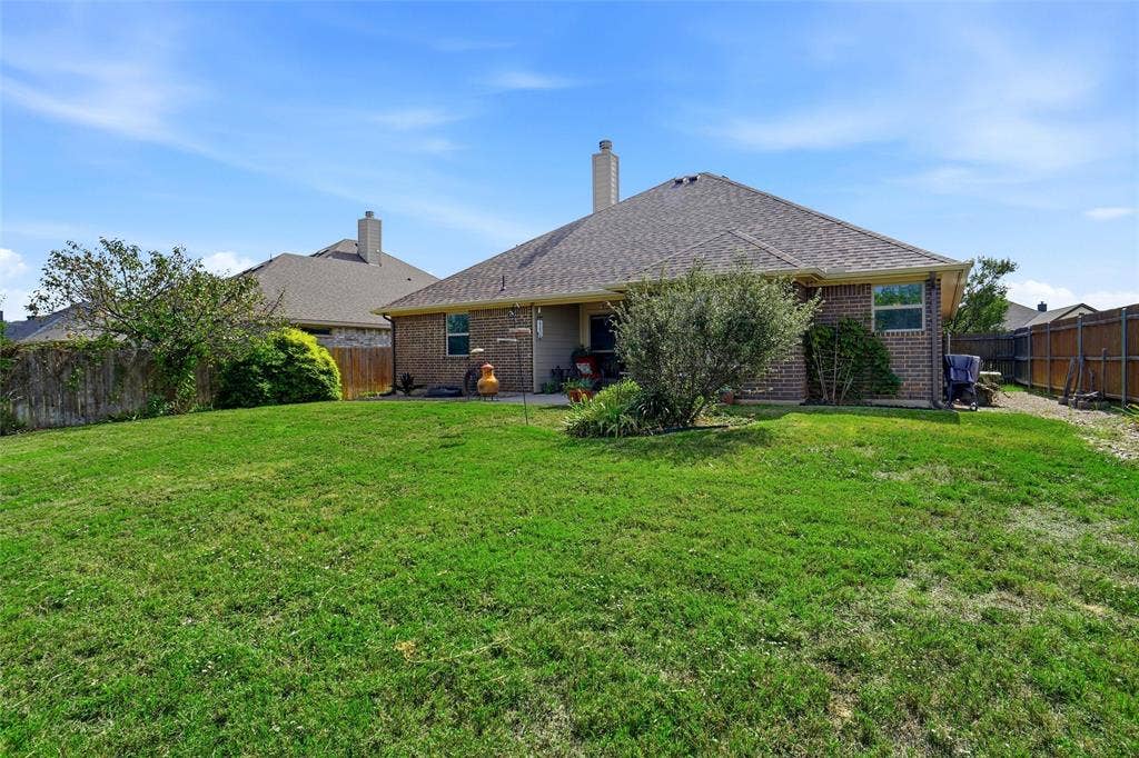 Brick exterior residence featuring a hipped roofline, a masonry chimney, a concrete patio, and a fenced backyard