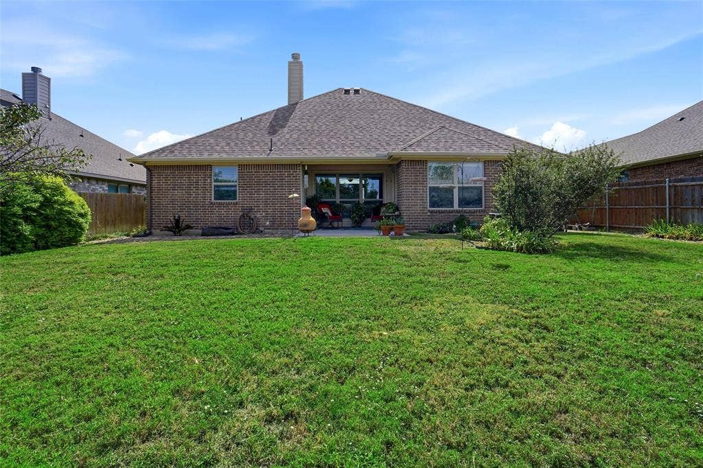 Expansive backyard featuring a manicured lawn, brick exterior, central chimney, concrete patio, and perimeter wood fencing