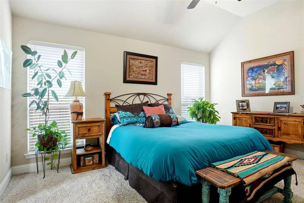Vaulted ceilings, neutral wall color, two windows with horizontal blinds, carpeted flooring, and a ceiling fan