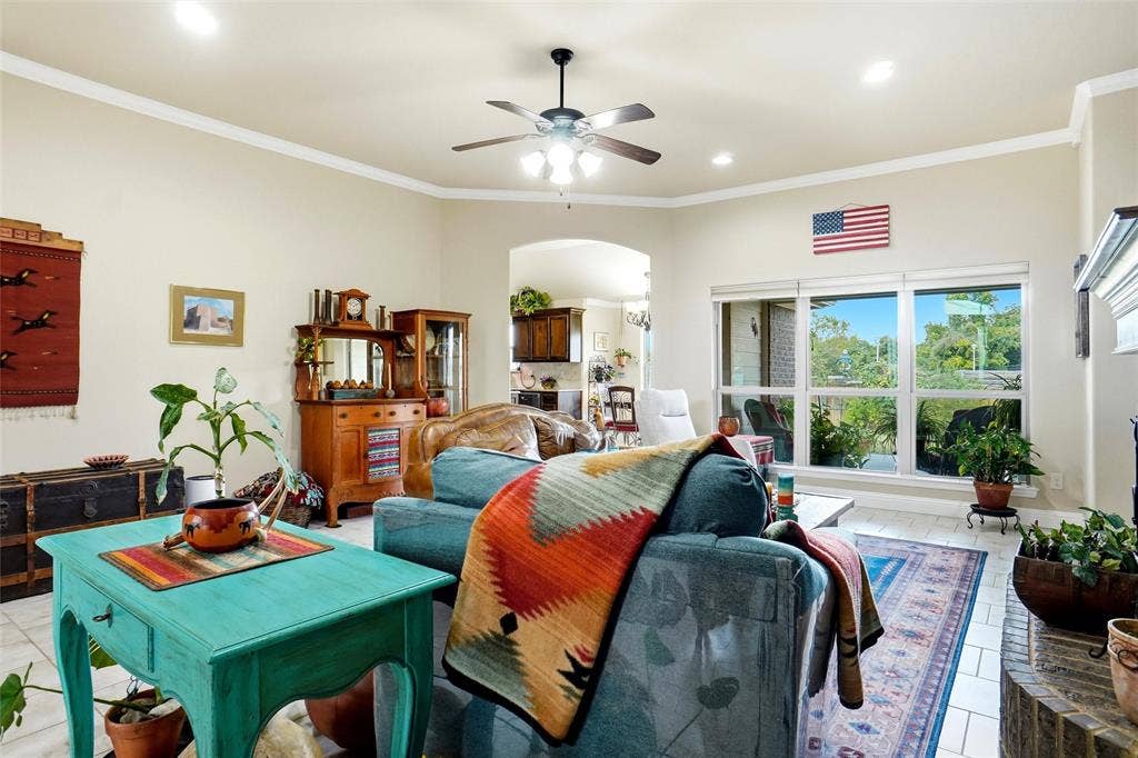 Spacious living area featuring neutral wall tones, crown molding, tile flooring, a multi-blade ceiling fan, and large windows