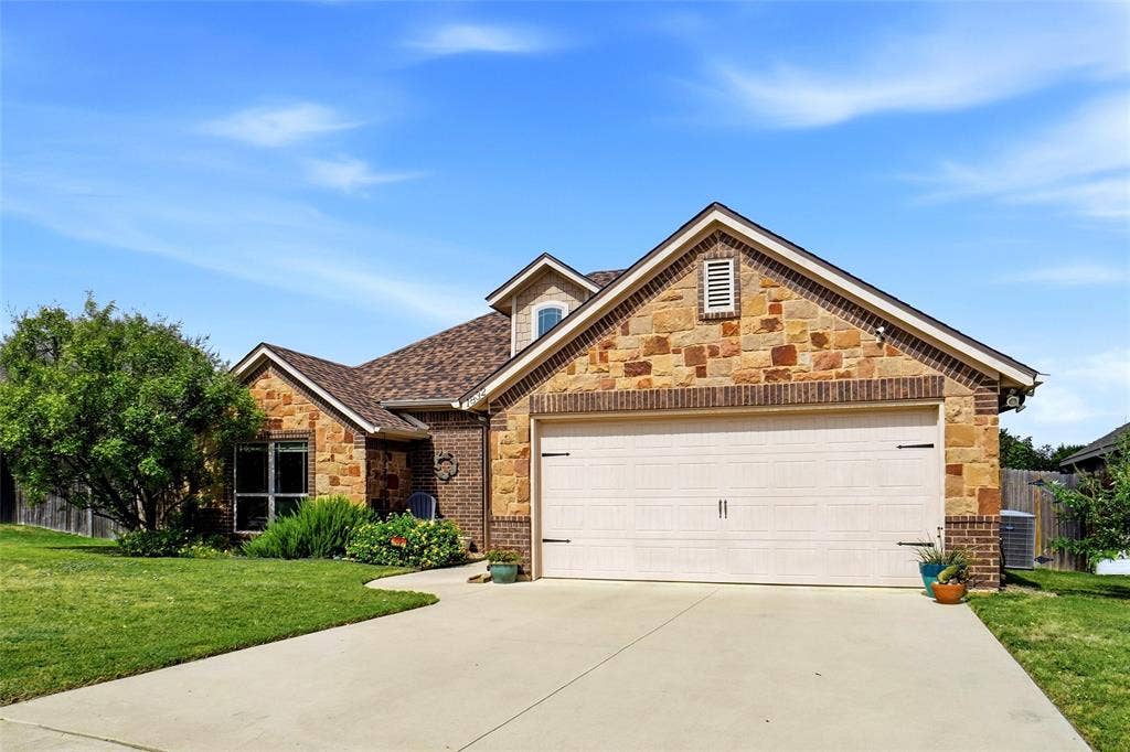 Exterior featuring a stone and brick facade, a multi-gabled roofline, and an attached multi-car garage with a concrete driveway