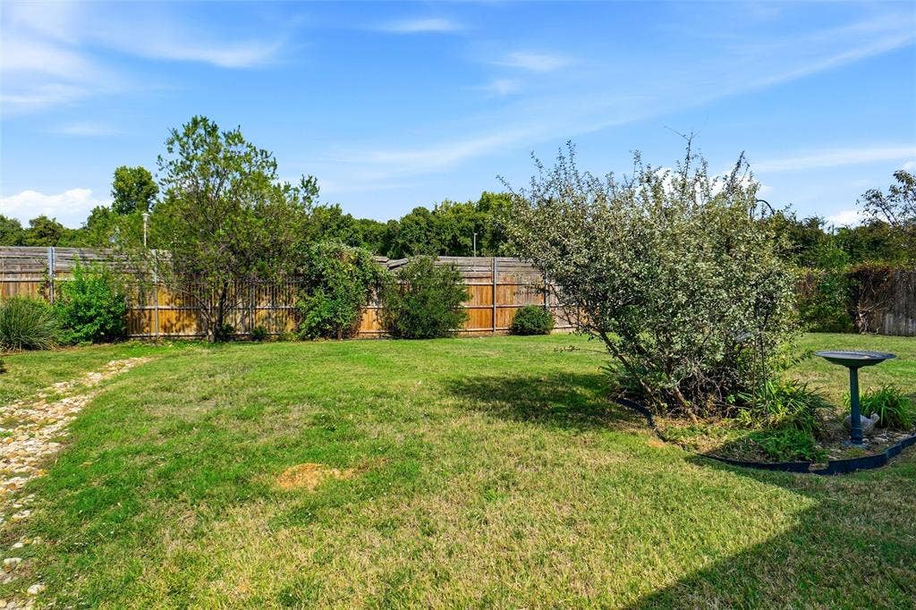 Backyard featuring a grass lawn, mature trees, wood privacy fencing, and stone-accented walkway