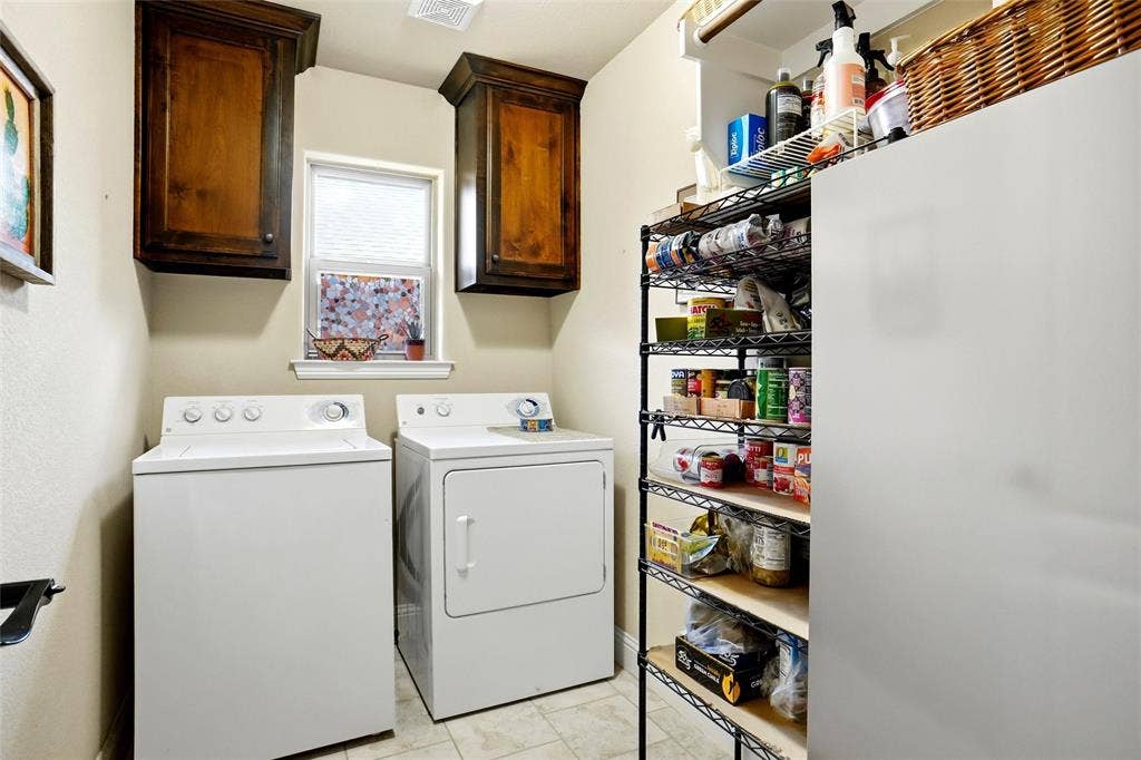 Laundry area featuring dark wood-finish wall cabinetry, neutral tile flooring, and a window providing natural illumination