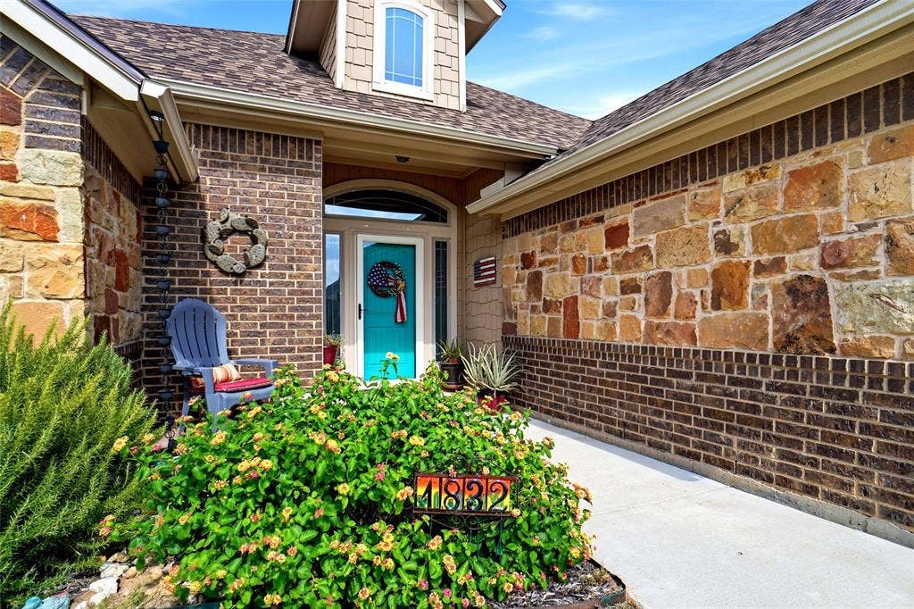 Exterior facade featuring a combination of natural stone veneer and brick masonry, an arched entryway, a dormer window, and a concrete walkway
