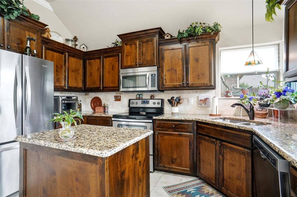 Kitchen featuring stained wood cabinetry, stone countertops, stainless steel appliances, a central island, and a dual-basin sink with a pull-down faucet