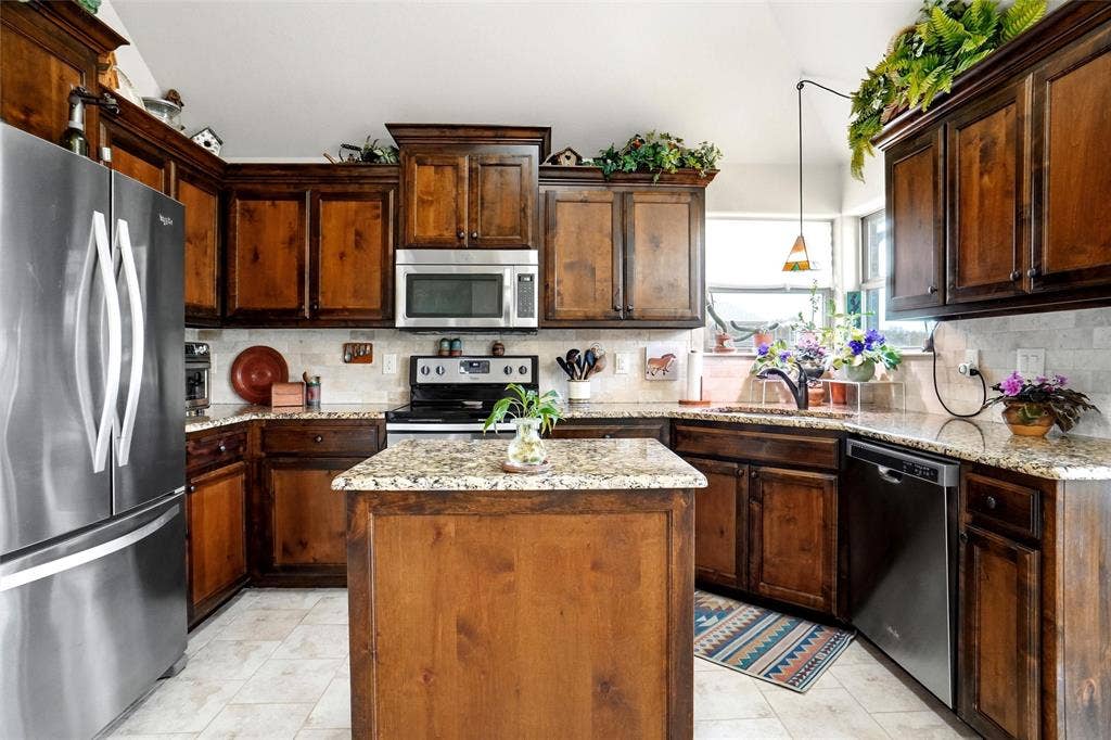 Kitchen featuring stained wood cabinetry, stone-surface countertops, central island, tiled backsplash, and stainless steel appliances