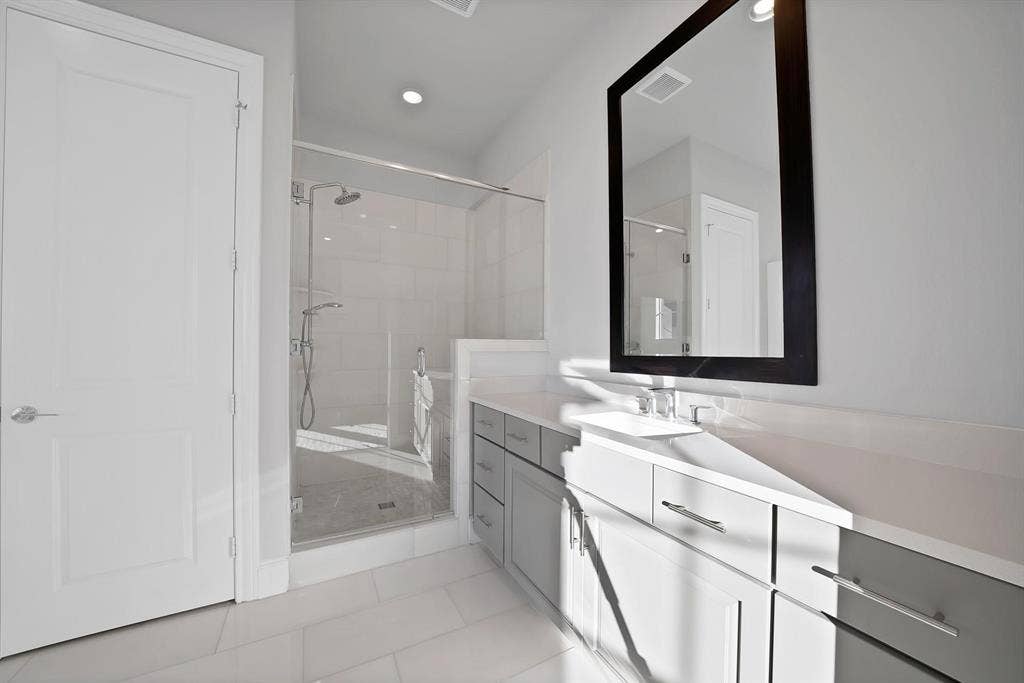 Full-height tiled shower with glass enclosure, dual shower heads, double vanity with white countertops, and contemporary gray cabinetry