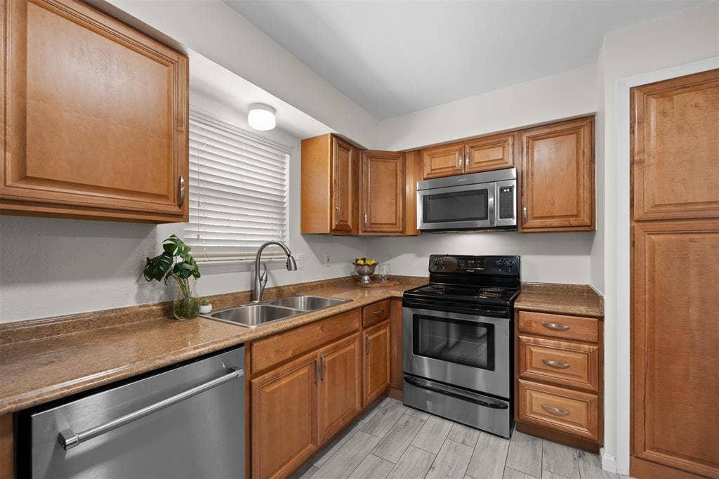 1118 Pacific Drive, Richardson, TX 75081 Kitchen featuring wood cabinetry, stainless steel appliances, dual basin sink, and wood-finish flooring