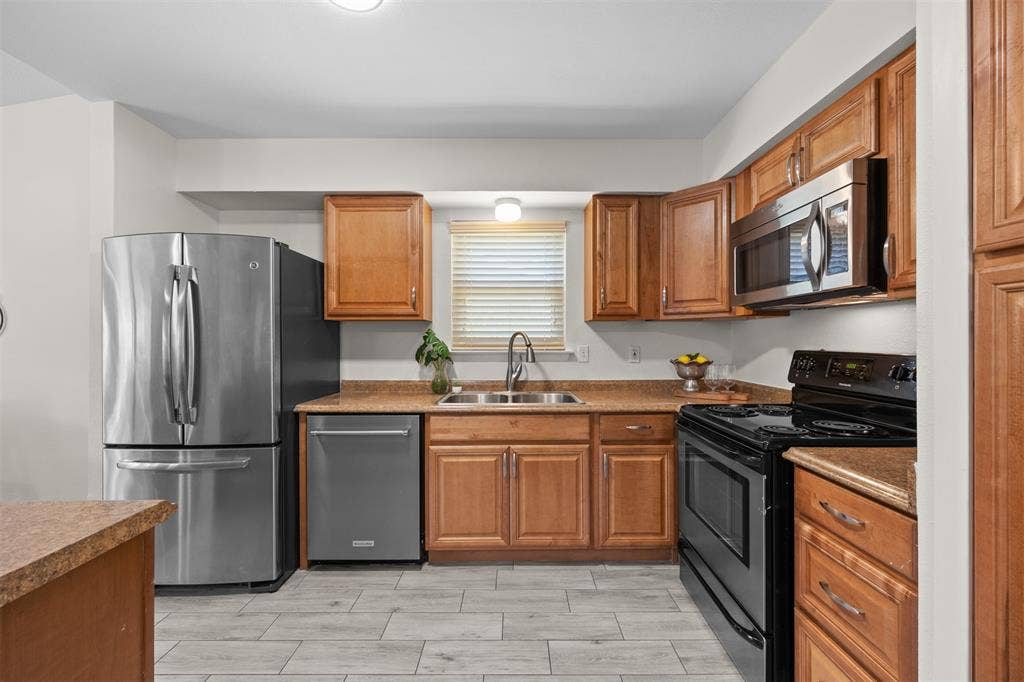 1118 Pacific Drive, Richardson, TX 75081 Kitchen featuring wood cabinetry, stainless steel appliances, a black range, a double basin sink, and wood-finish flooring