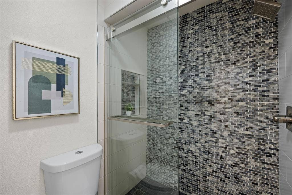 1118 Pacific Drive, Richardson, TX 75081 Glass-enclosed shower with mosaic tile surround, rainfall showerhead, and a fixed toilet