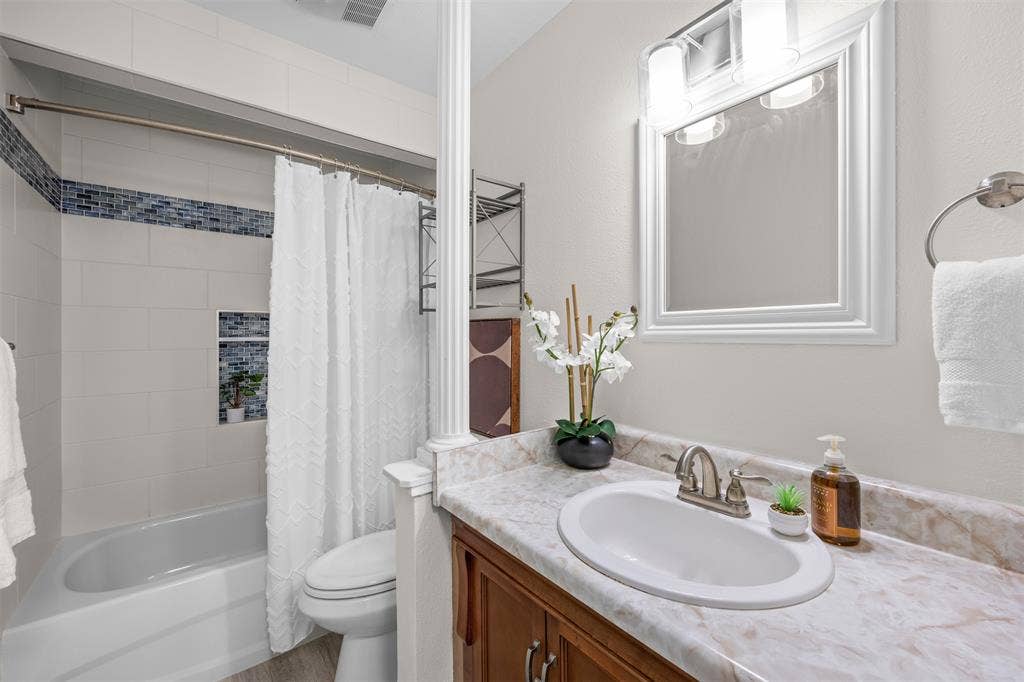 1118 Pacific Drive, Richardson, TX 75081 Vanity with an integrated sink and light-toned countertop, wood-finish cabinetry, and a framed mirror with an overhead vanity light