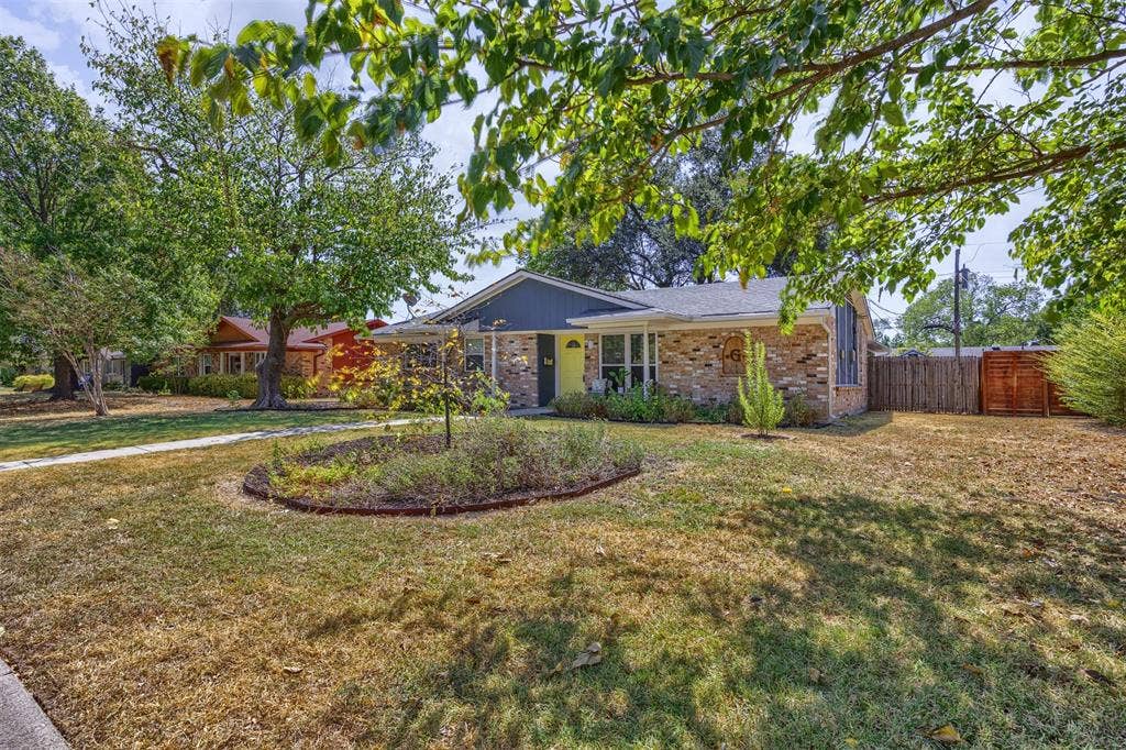 1118 Pacific Drive, Richardson, TX 75081 Brick exterior with a contrasting façade, a central landscaped garden bed, mature trees, and a privacy fence