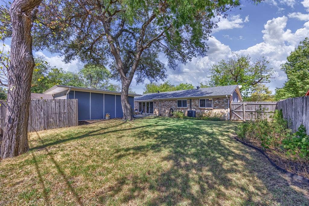 1118 Pacific Drive, Richardson, TX 75081 Expansive backyard featuring a manicured lawn, mature shade trees, and a wooden privacy fence