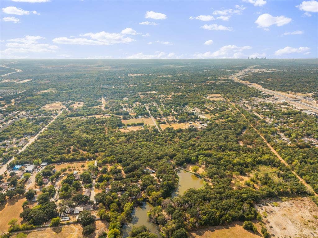 19 No Name Street, Dallas, TX 75217 Expansive aerial showcasing a verdant landscape with mature trees, a natural pond, and distant roadways