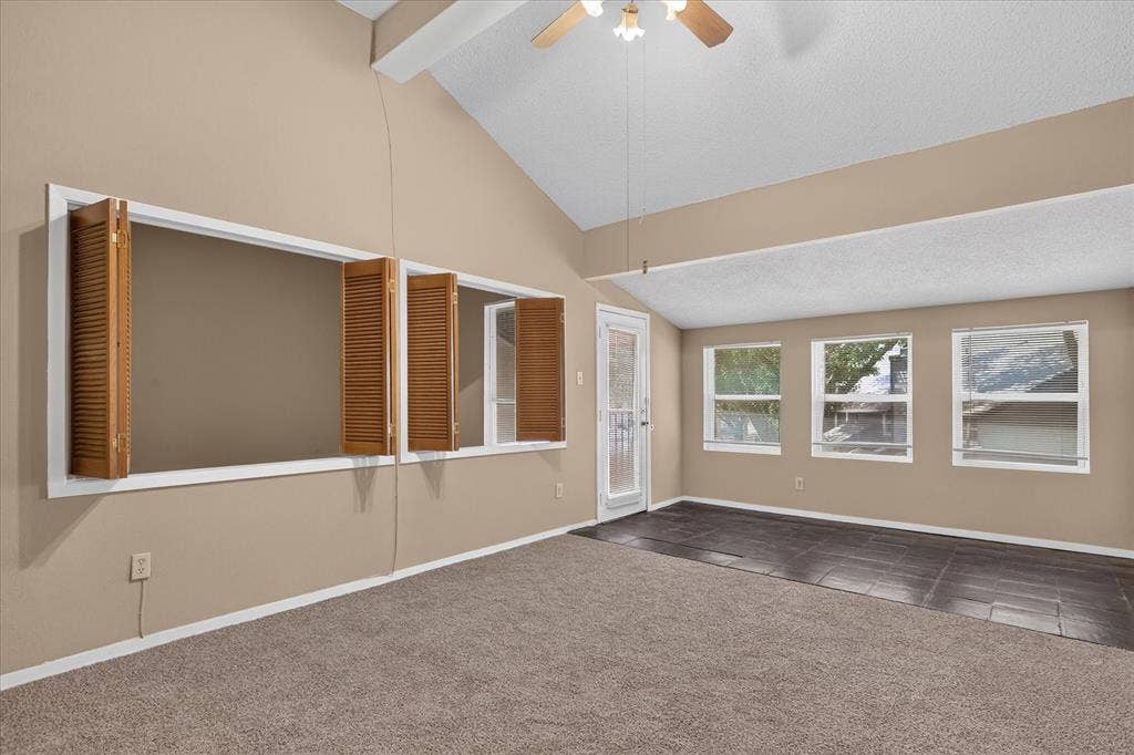 Vaulted ceiling with ceiling fan, large interior window with wood shutters, multiple exterior windows, tile flooring, and carpet flooring