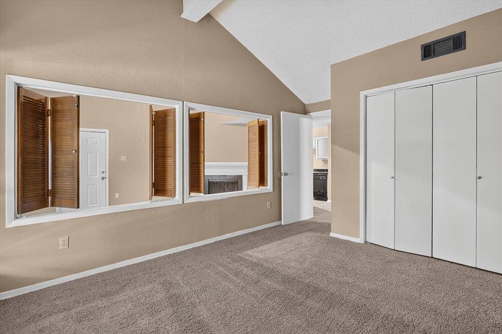 Vaulted ceiling, neutral tone walls, carpeted flooring, bi-fold closet doors, and interior shutters