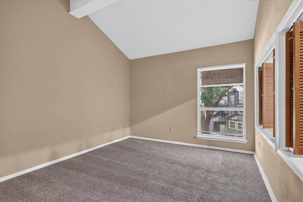 Vaulted ceiling, neutral wall tones, gray carpet, double-hung window, and wooden louvered shutters