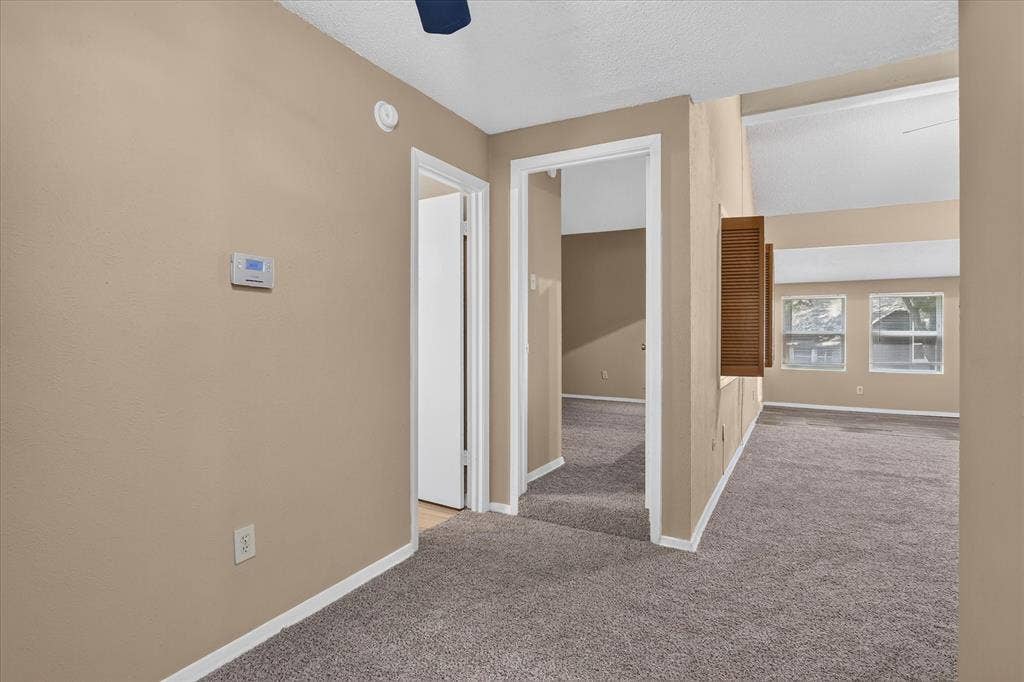 Vaulted ceiling, multiple windows, textured tan walls, white trim, and gray carpet flooring