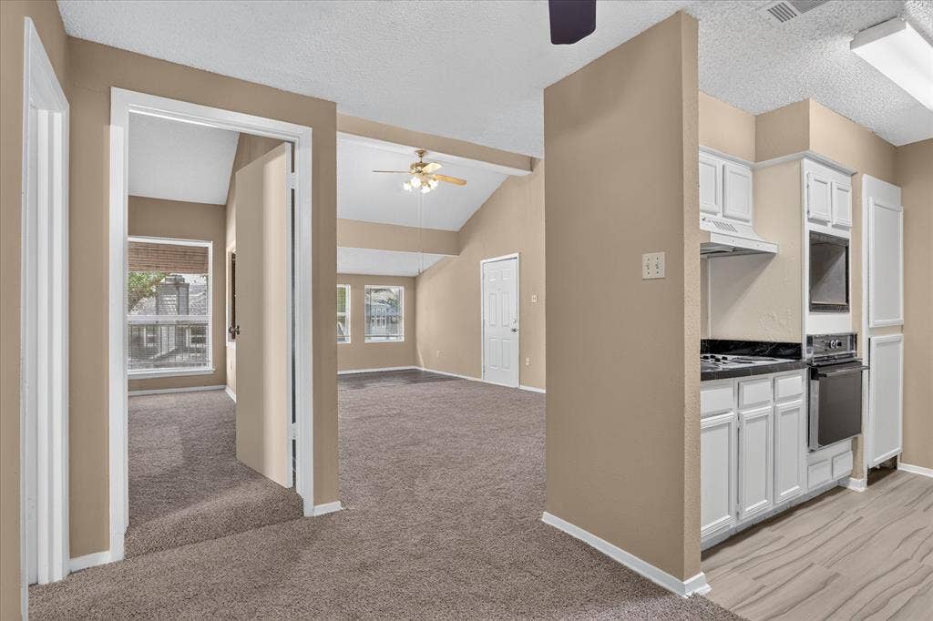 Vaulted ceilings, a ceiling fan, white kitchen cabinetry, dark countertops, and wood-finish flooring