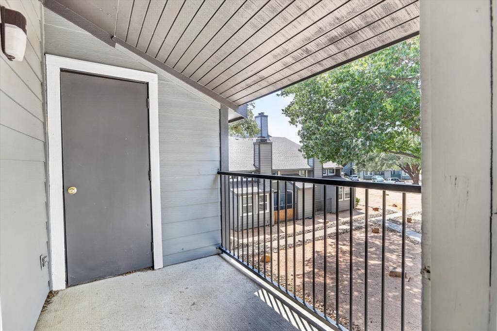 Covered outdoor balcony with concrete flooring, accented by a black metal railing