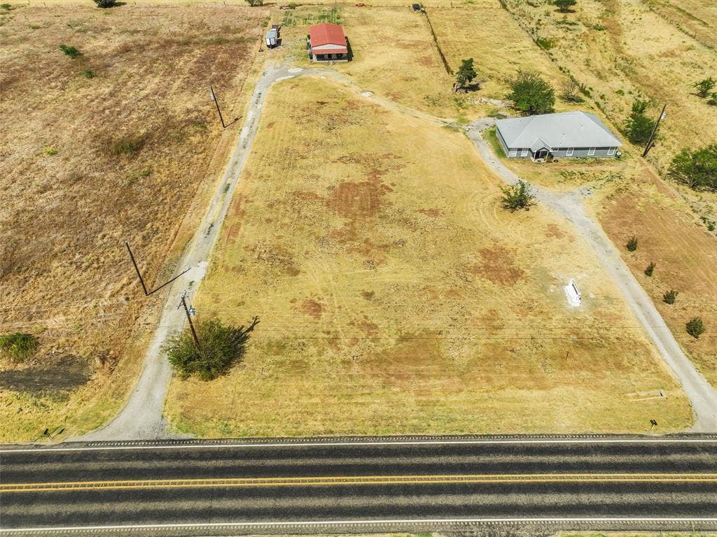 16880 W Fm 455, Celina, TX 75009 Expansive rural property featuring a single-story residence with a gray roof, a separate red-roofed outbuilding, and direct road frontage