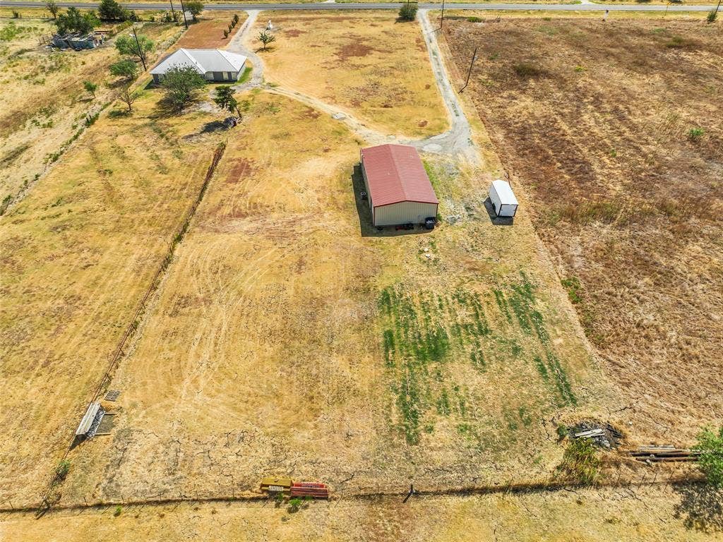 16880 W Fm 455, Celina, TX 75009 Expansive land parcel featuring a residential structure, a large outbuilding with a red roof, and an additional smaller white outbuilding