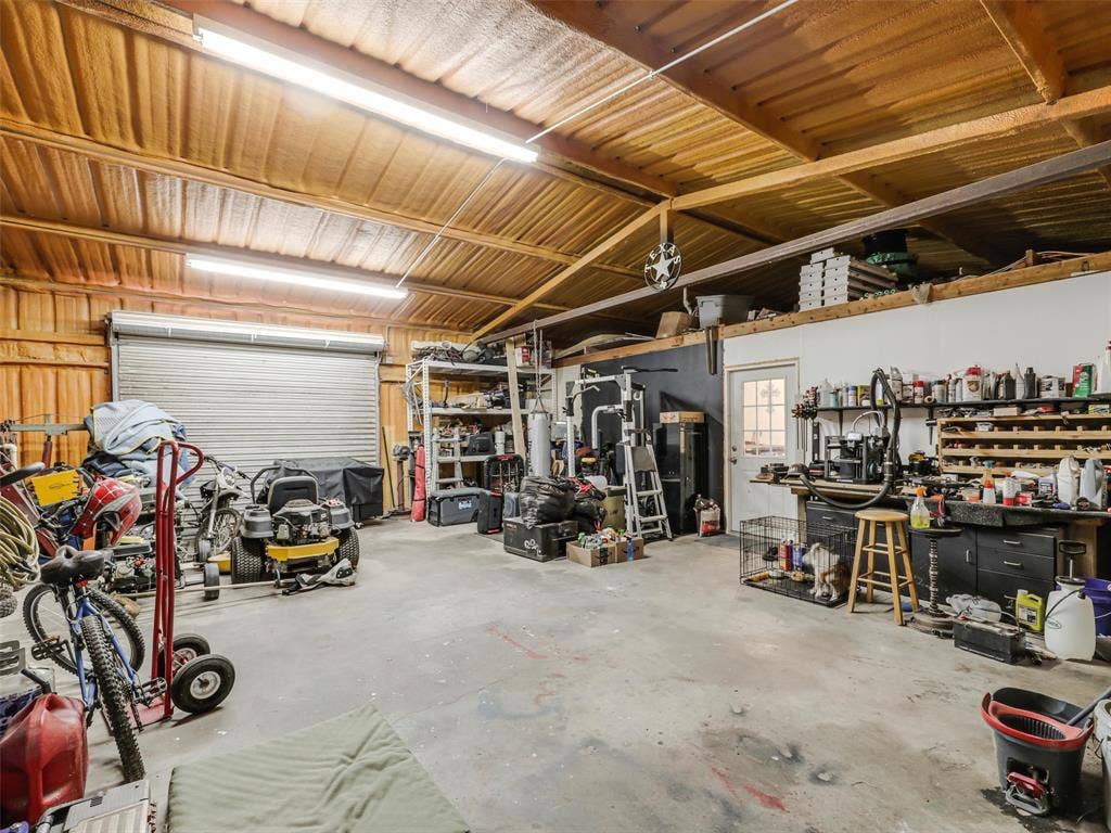 16880 W Fm 455, Celina, TX 75009 Spacious garage featuring a roll-up door, exposed wood beam ceiling, concrete flooring, and built-in shelving