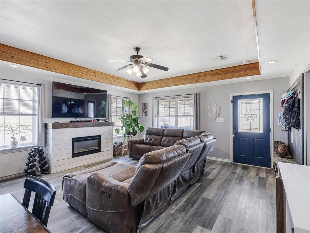 16880 W Fm 455, Celina, TX 75009 Recessed ceiling with wood beams, electric fireplace with white shiplap surround, wood-finish flooring, ceiling fan, and multiple windows