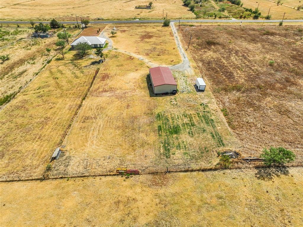 16880 W Fm 455, Celina, TX 75009 Expansive land parcel featuring a residential structure, a large outbuilding with a red roof, a detached utility structure, and established perimeter fencing