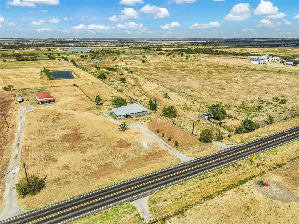 16880 W Fm 455, Celina, TX 75009 Expansive rural property featuring a primary residence, an additional auxiliary structure with a red roof, a pond, and a paved road frontage
