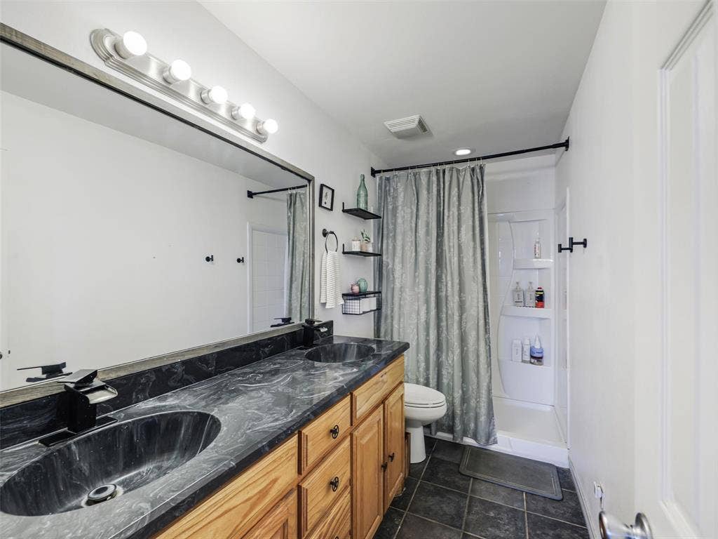 16880 W Fm 455, Celina, TX 75009 Dual vanity with a dark countertop and undermount sinks, wood cabinetry, large vanity mirror, and dark tile flooring