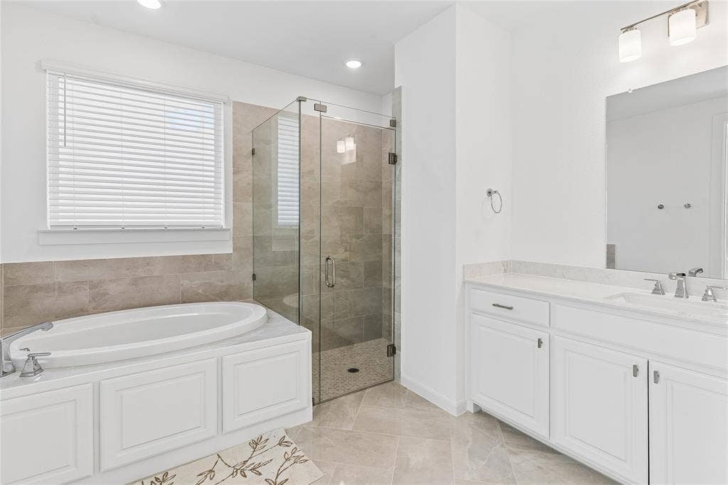 Soaking tub with white cabinetry, glass-enclosed shower, dual vanity with undermount sinks, and tile flooring