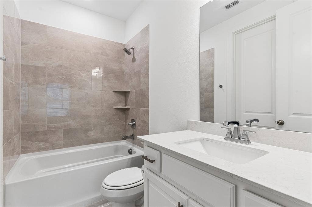 Shower/tub combination with tile surround, white vanity with integrated sink, chrome fixtures, and white cabinetry
