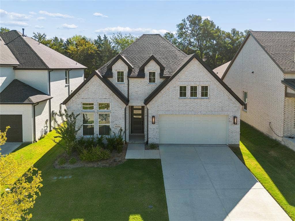 White brick exterior with dark trim accents, a two-car garage, and a concrete driveway