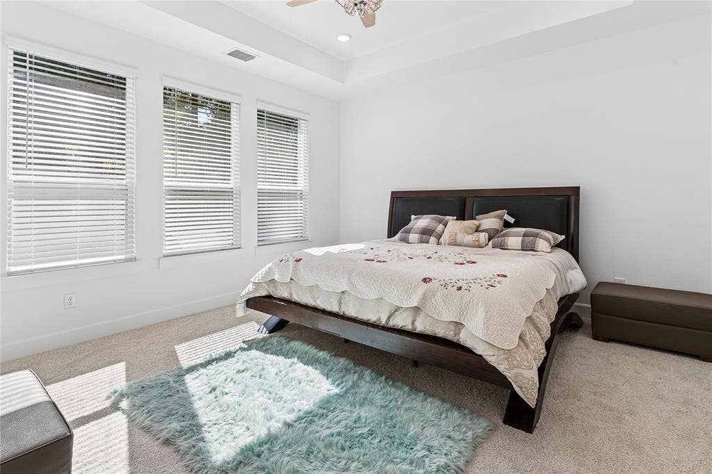 Tray ceiling with recessed lighting, ceiling fan, three windows with blinds, and carpeted flooring