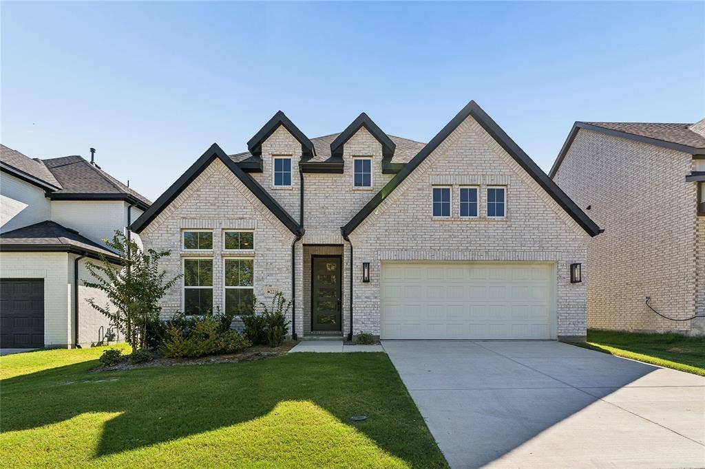 White brick exterior with dark trim accents, attached two-car garage, multiple gabled rooflines, and a paved driveway