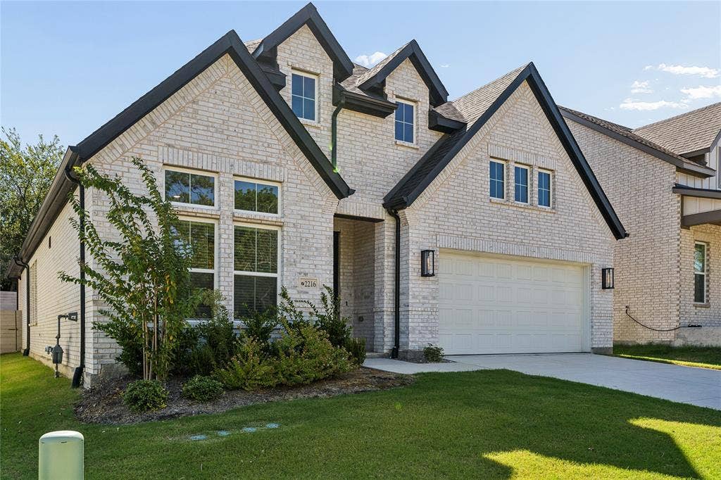 Light-colored brick exterior with dark trim accents, multiple gables, an attached garage, a concrete driveway, and landscaping