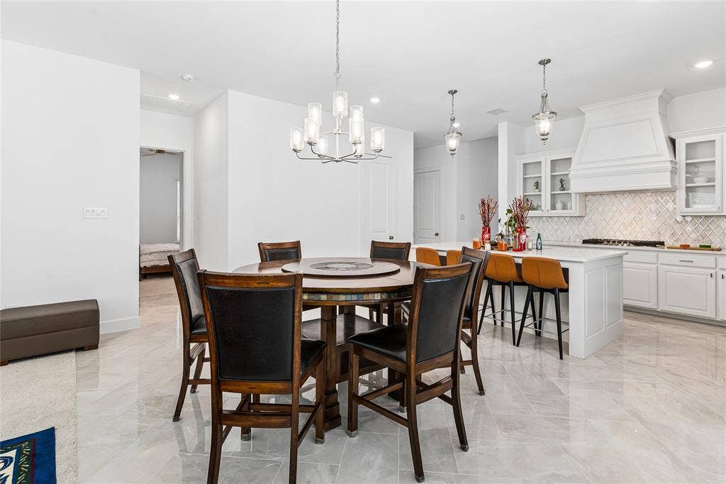 Open-concept kitchen and dining area with light-toned tile flooring, recessed lighting, and a chandelier