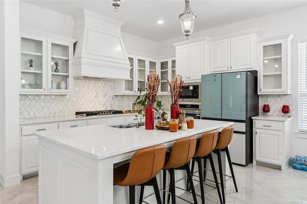 White cabinetry with glass-front display uppers, quartz countertops, a diamond-patterned tile backsplash, and a large center island