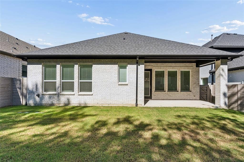 Exterior featuring light brick construction, a covered patio, a dark shingle roof, and multiple windows