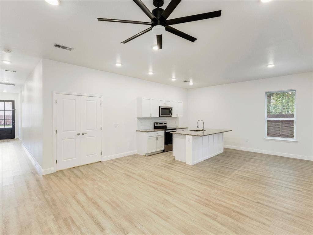 82 Indian Harbor Drive, Mabank, TX 75156 Wood-finish flooring, recessed lighting, and a modern ceiling fan complement the white kitchen cabinetry, stainless steel appliances, and kitchen island with a sink