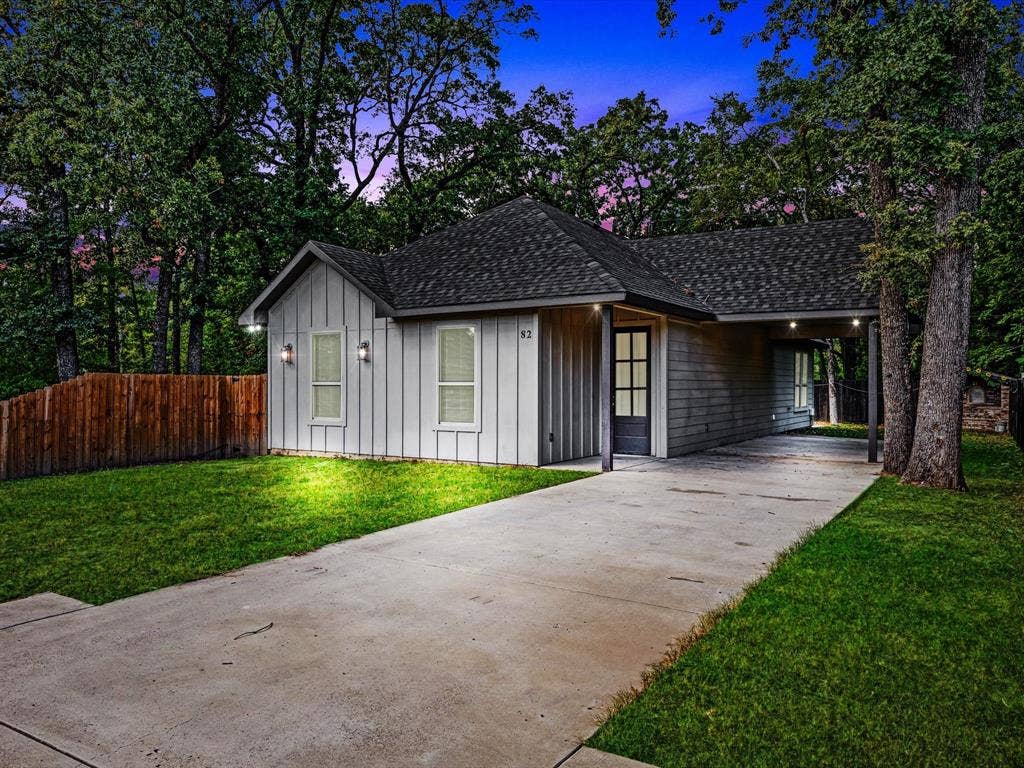 82 Indian Harbor Drive, Mabank, TX 75156 Gable roofline with dark shingles, light vertical board and batten siding, dark framed windows, covered carport, and wood privacy fencing