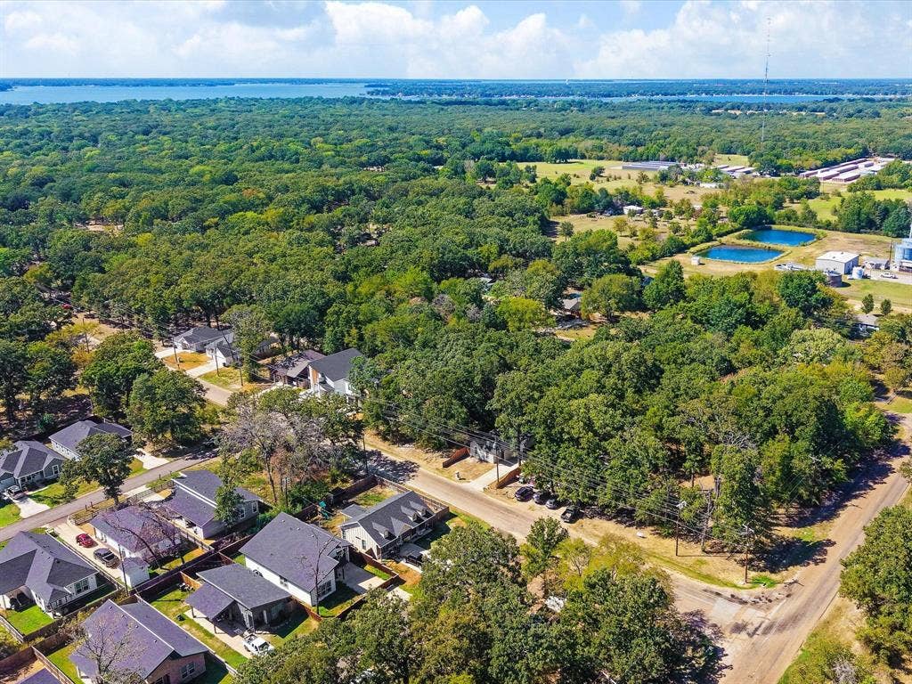 82 Indian Harbor Drive, Mabank, TX 75156 Aerial perspective showcasing abundant mature trees, residential properties with dark roofs, and a distant body of water