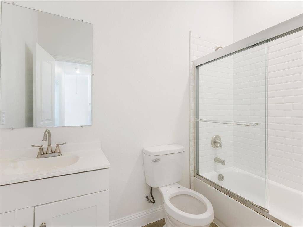 82 Indian Harbor Drive, Mabank, TX 75156 Bathroom featuring a white vanity with integrated sink, brushed nickel faucet, wall-mounted mirror, toilet, and a shower-tub combination with sliding glass doors and white subway tile surround