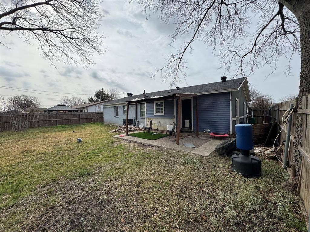 Rear exterior with blue siding, a covered patio, a concrete patio area, and a wood privacy fence