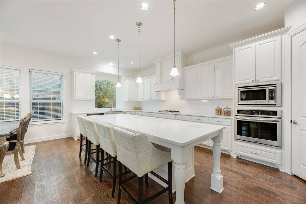 2408 Brisbane Lane, Plano, TX 75075 Expansive kitchen featuring a large central island, white cabinetry, integrated stainless steel appliances, dark wood-finish flooring, and recessed lighting