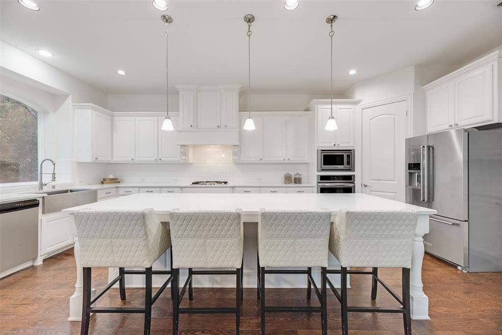 2408 Brisbane Lane, Plano, TX 75075 White shaker cabinetry with crown molding, stainless steel appliances, a center island with pendant lighting, and wood-finish flooring