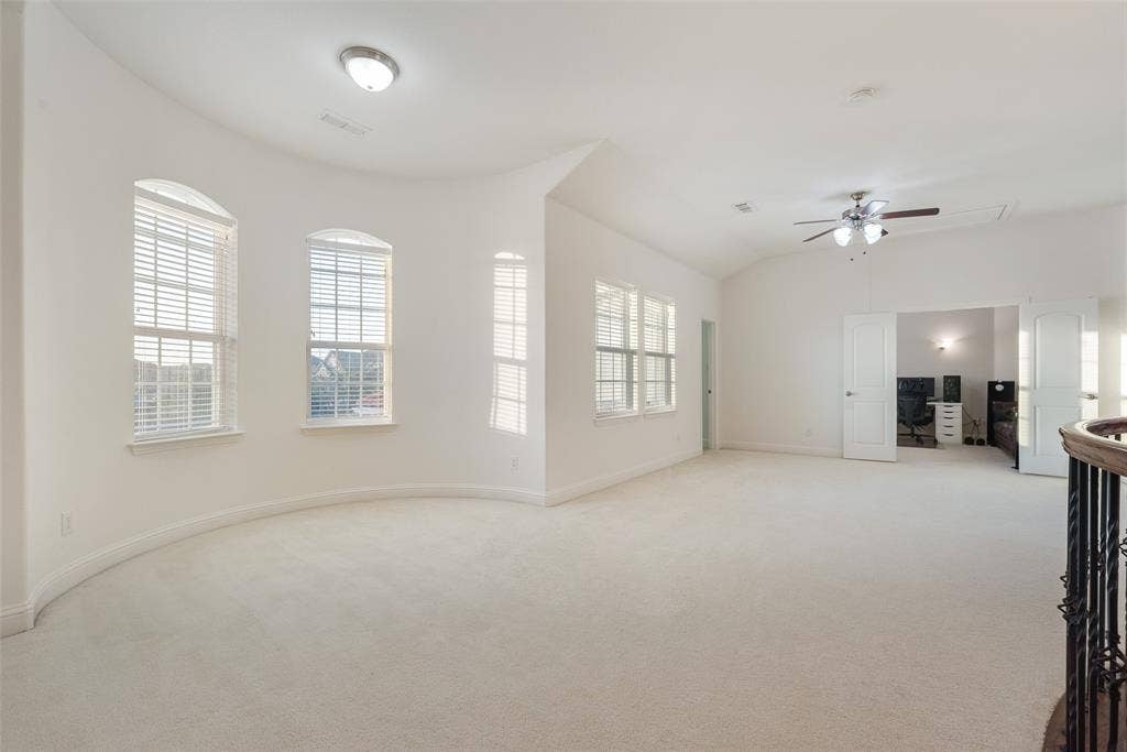 2408 Brisbane Lane, Plano, TX 75075 Spacious carpeted room featuring a vaulted ceiling with a ceiling fan, multiple windows with blinds, and a built-in archway leading to an additional space